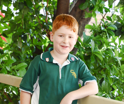 A stage 1 student standing in front of a tree on the verandah.