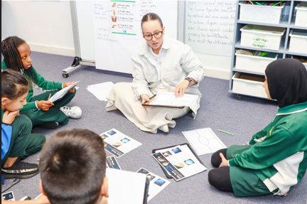 Teacher working with a group of students on the floor in a bright classroom.