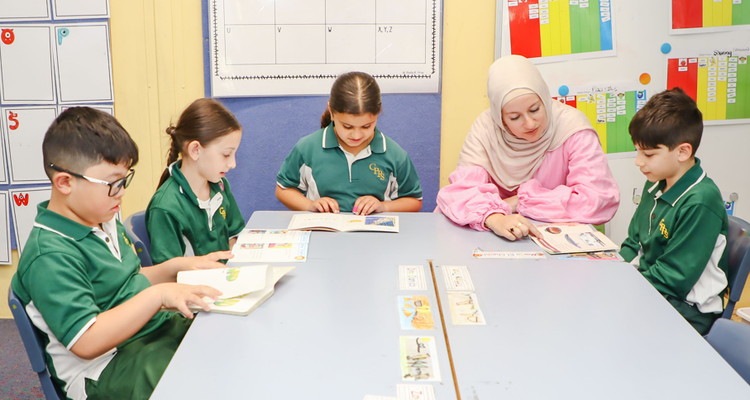 four students sitting at a table receiving support in reading from a teacher.