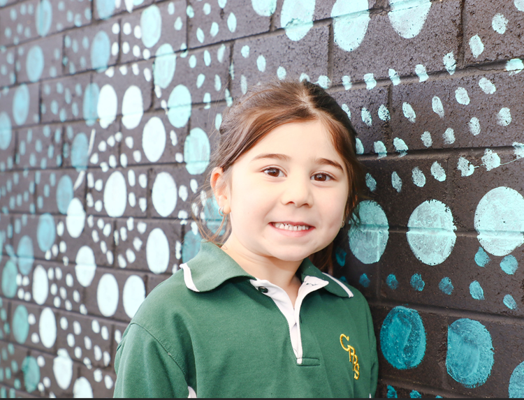 Kindergarten student beside an Aboriginal themes mural.