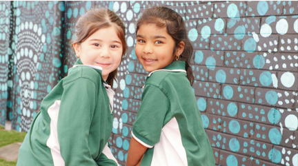 Two kindergarten students sitting in front of a mural.